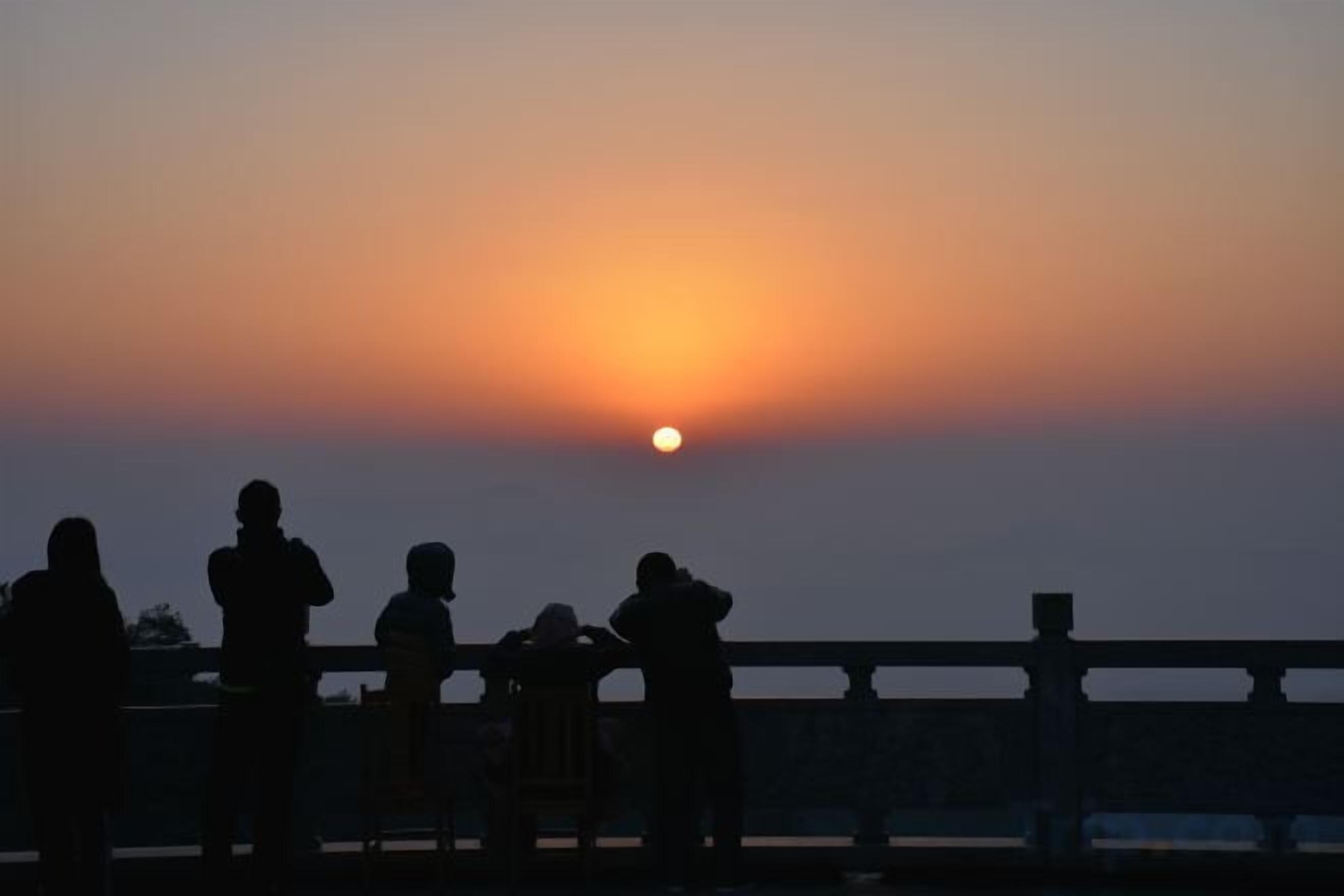 Un tramonto con le sagome di persone su un ponte.