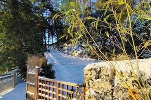 Un sendero cubierto de nieve que atraviesa una zona boscosa con un portón de madera y un muro de piedra.