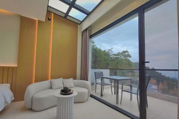 A modern room with a sofa, a small round table, and a balcony with a glass door. - Mountain and Courtyard Homestay (Hengyang)