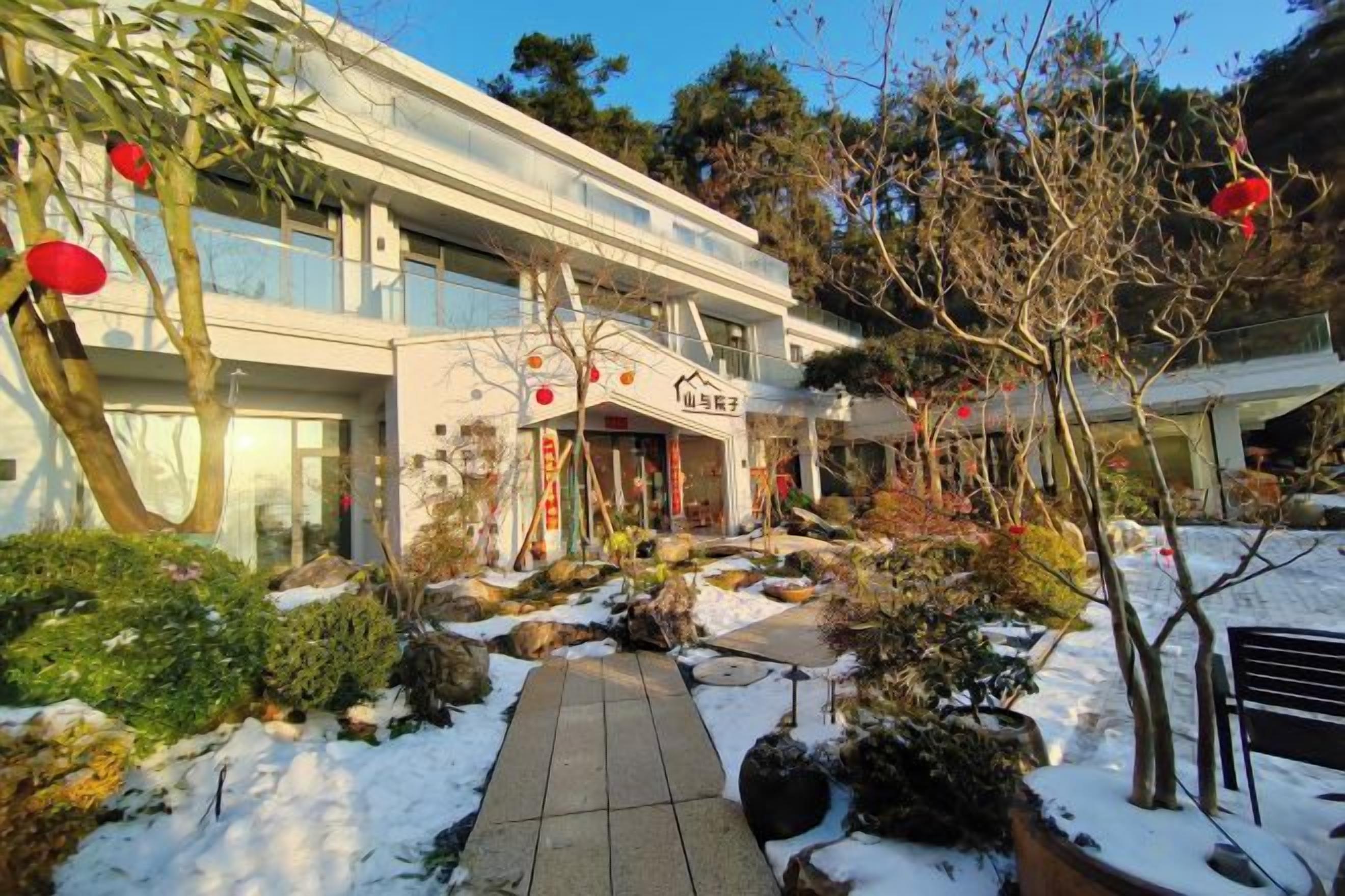 Un edificio con estilo arquitectónico tradicional, un sendero cubierto de nieve y un jardín bien cuidado con rocas y arbustos.