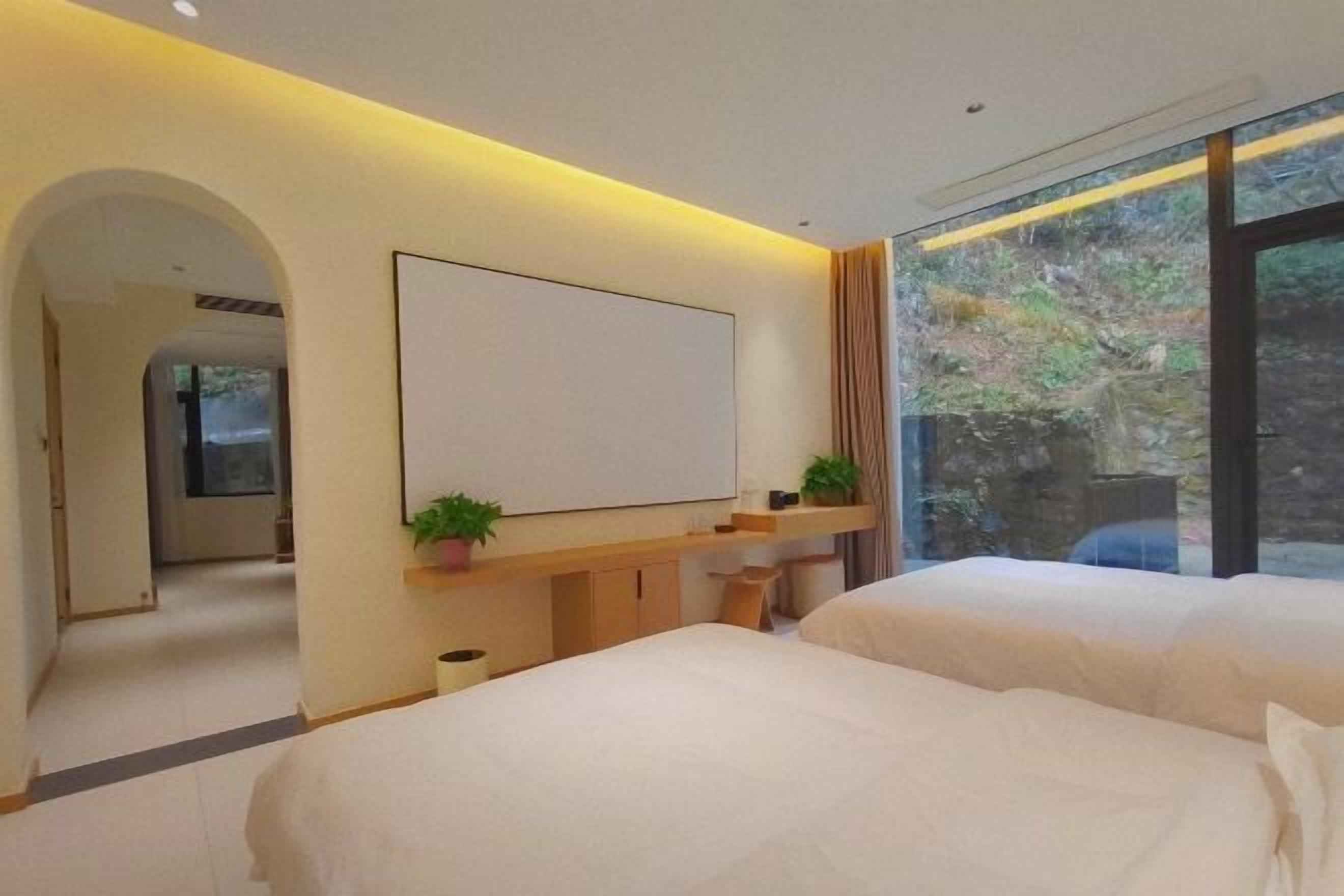 Une chambre d’hôtel moderne, dotée de deux lits, d’un grand miroir, d’un téléviseur à écran plat et d’une fenêtre donnant sur un paysage verdoyant.