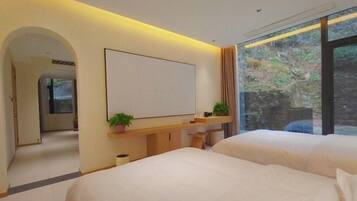Une chambre d’hôtel moderne, dotée de deux lits, d’un grand miroir, d’un téléviseur à écran plat et d’une fenêtre donnant sur un paysage verdoyant.