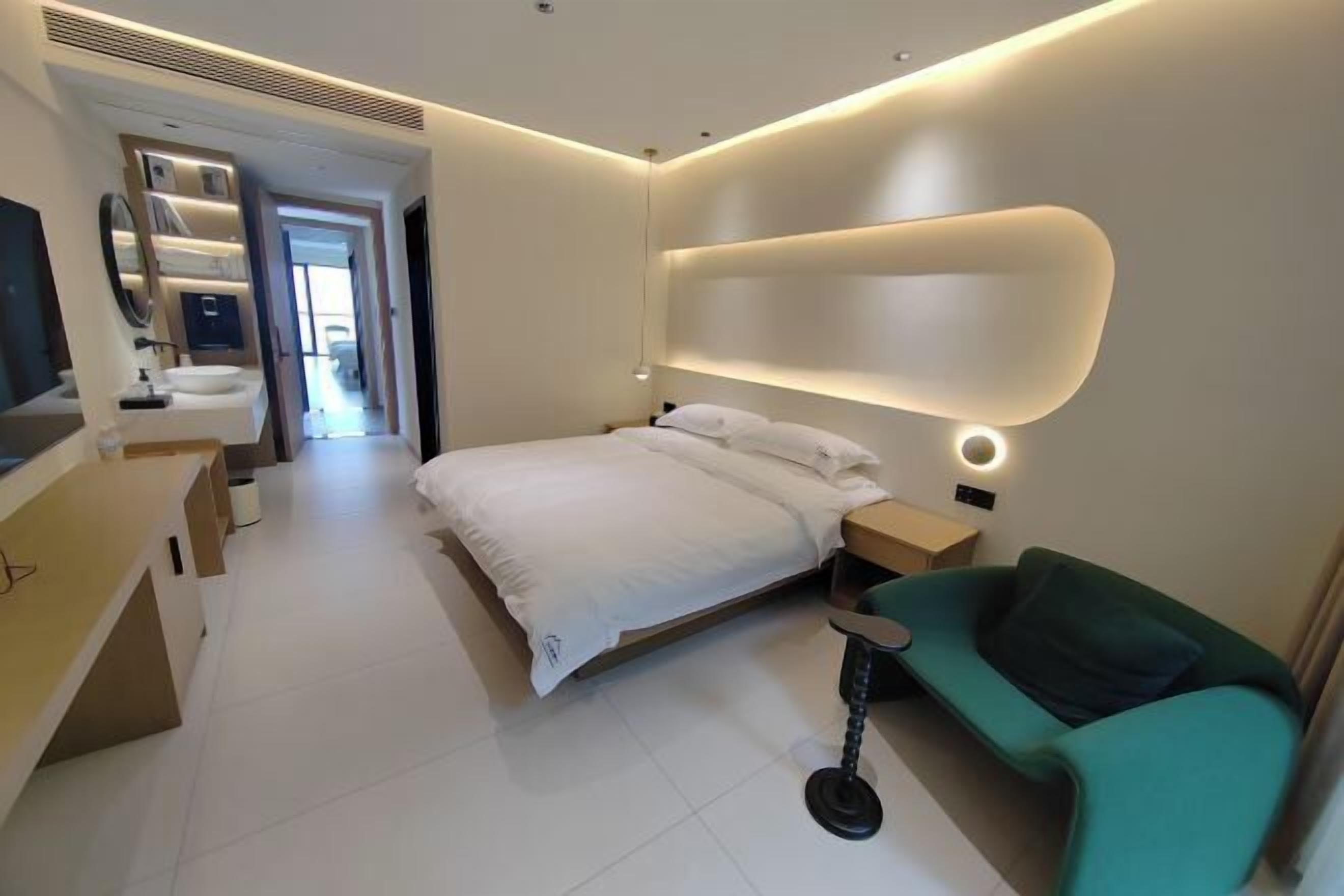 A modern bedroom with a bed, bedside table, and a green armchair.