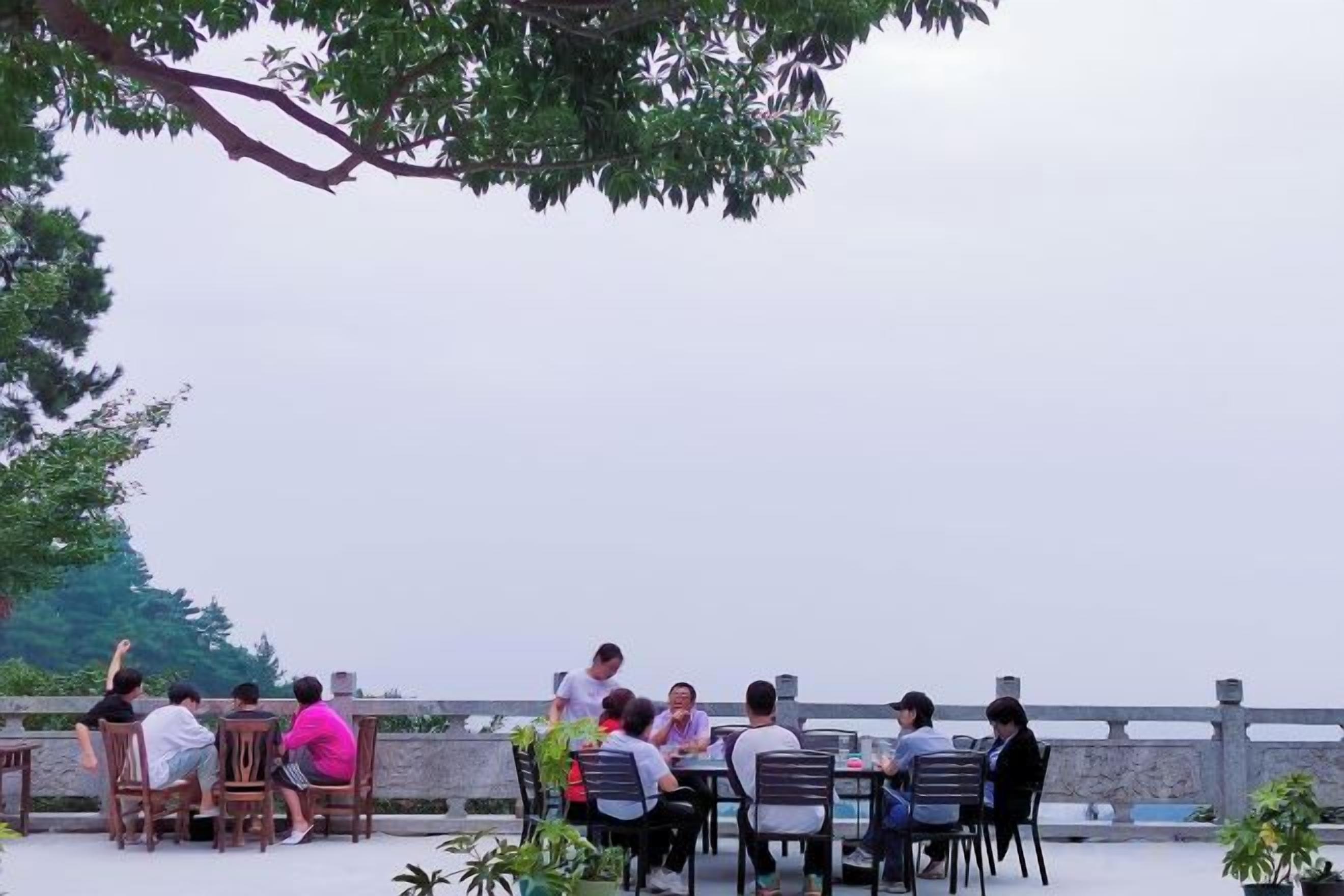 A group of people seated at tables outdoors with a view of a body of water.