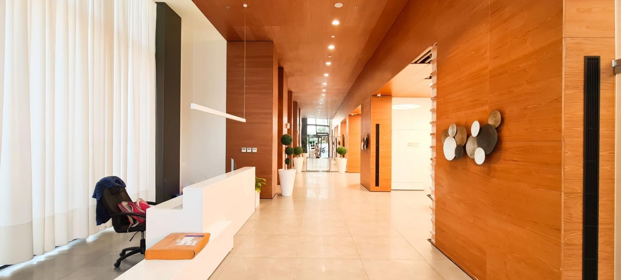 A modern hotel lobby with a reception desk, a waiting area with chairs, and a hallway leading to other rooms.