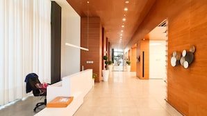 Un vestíbulo de hotel moderno con una recepción, un área de espera con sillas y un pasillo que conduce a otras habitaciones.