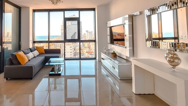 Un salón moderno con un sofá grande, una mesa de centro y vistas a la ciudad a través de amplios ventanales.