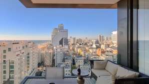 Un balcón con vistas a la ciudad, una mesa con una botella y un sofá.