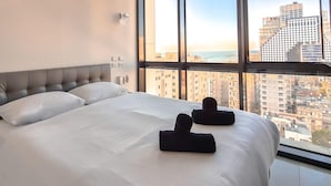 Habitación de hotel con una cama grande, vistas a un paisaje urbano a través de amplias ventanas y un diseño moderno.