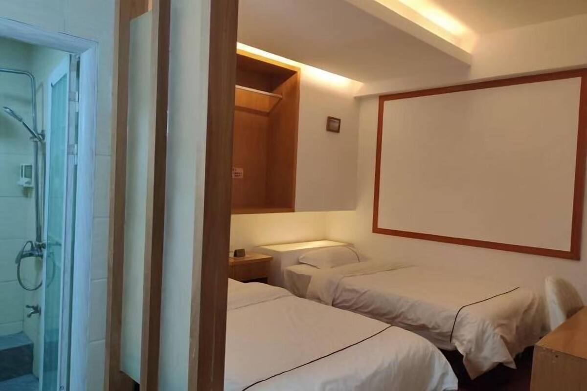 Habitación de hotel con ducha, dos camas, una mesita de noche y un espejo grande.