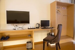 Una habitación con televisión, computadora, silla, cafetera y perchero.