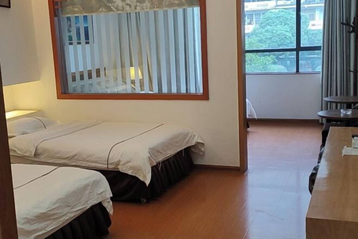 Una habitación con dos camas, un escritorio de madera, una ventana con persianas y vistas a edificios.