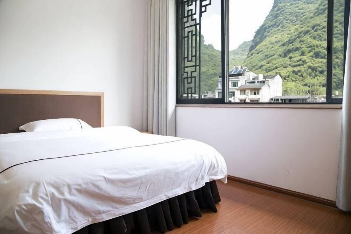 Una habitación de hotel con cama, ventana que ofrece vistas a una montaña y edificios, y piso de madera.