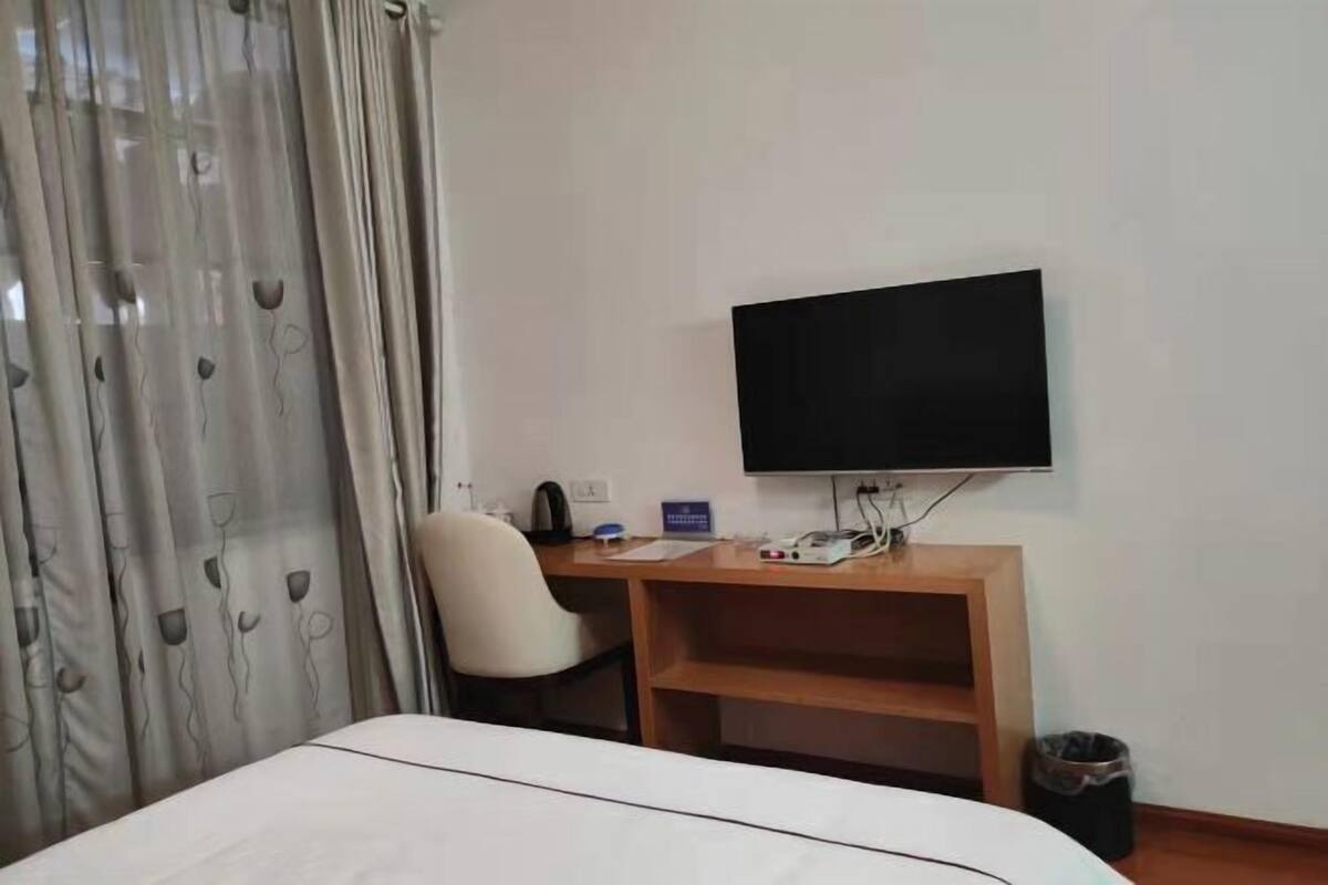 Habitación de hotel con cama, escritorio con computadora, silla, televisor montado en la pared y cortina con estampado floral.