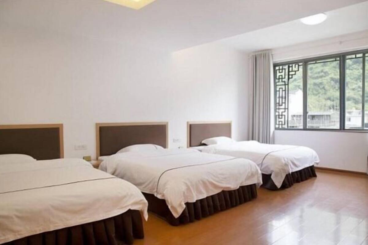 Una habitación de hotel con tres camas, un ventanal con vistas y suelo de madera.
