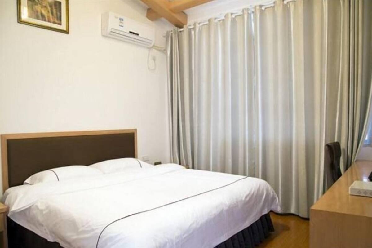 Habitación de hotel con cama, escritorio, silla, ventana con cortinas, equipo de aire acondicionado y teléfono instalado en la pared.