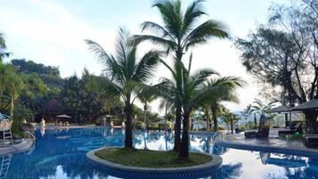 A swimming pool with palm trees, a lounge area, and a view of the surrounding landscape.