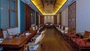 A long dining hall with wooden tables and chairs, a ceiling fan, and traditional decor. - Xinhe Resort (Hekou)