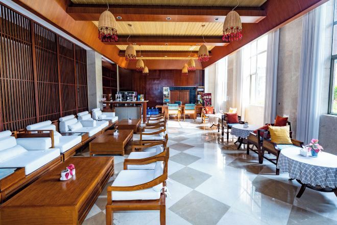 A hotel lobby with a checkered floor, wooden furniture, and a kitchen area in the background.