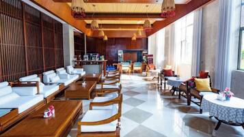 A hotel lobby with a checkered floor, wooden furniture, and a kitchen area in the background.