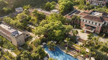 An aerial view of a hotel with a swimming pool surrounded by lush greenery and multiple buildings.