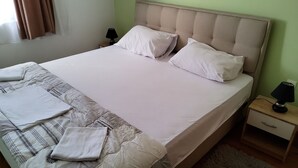 A neatly made bed with white linens, two pillows, and a matching blanket. There is a small bedside table with a lamp and a drawer. - Appealing Apartment 8 Sleeps 3 Guests (Split)
