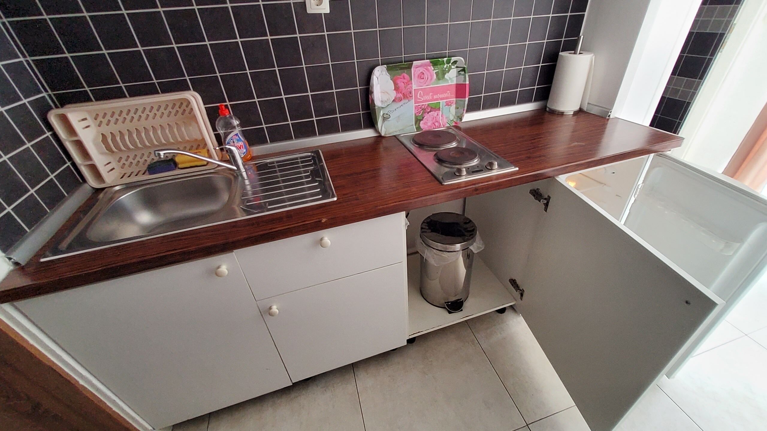 Een keuken met een spoelbak, een vergiet, een prullenbak en een rol keukenpapier.