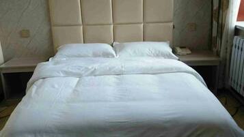 A bed with a padded headboard, a bedside table, and a nightstand.