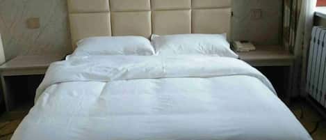 Una cama con cabecera acolchada, una mesita de noche y un velador.