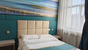 Une chambre d’hôtel avec un grand lit, une tête de lit, une table de chevet, une fenêtre avec des rideaux et un tableau représentant une scène de plage.