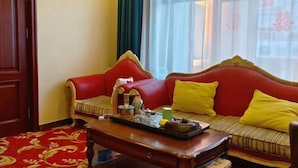 Une pièce avec un canapé rouge, une table basse en bois sur laquelle se trouve un plateau avec divers objets, une moquette à motifs et une fenêtre avec des rideaux.