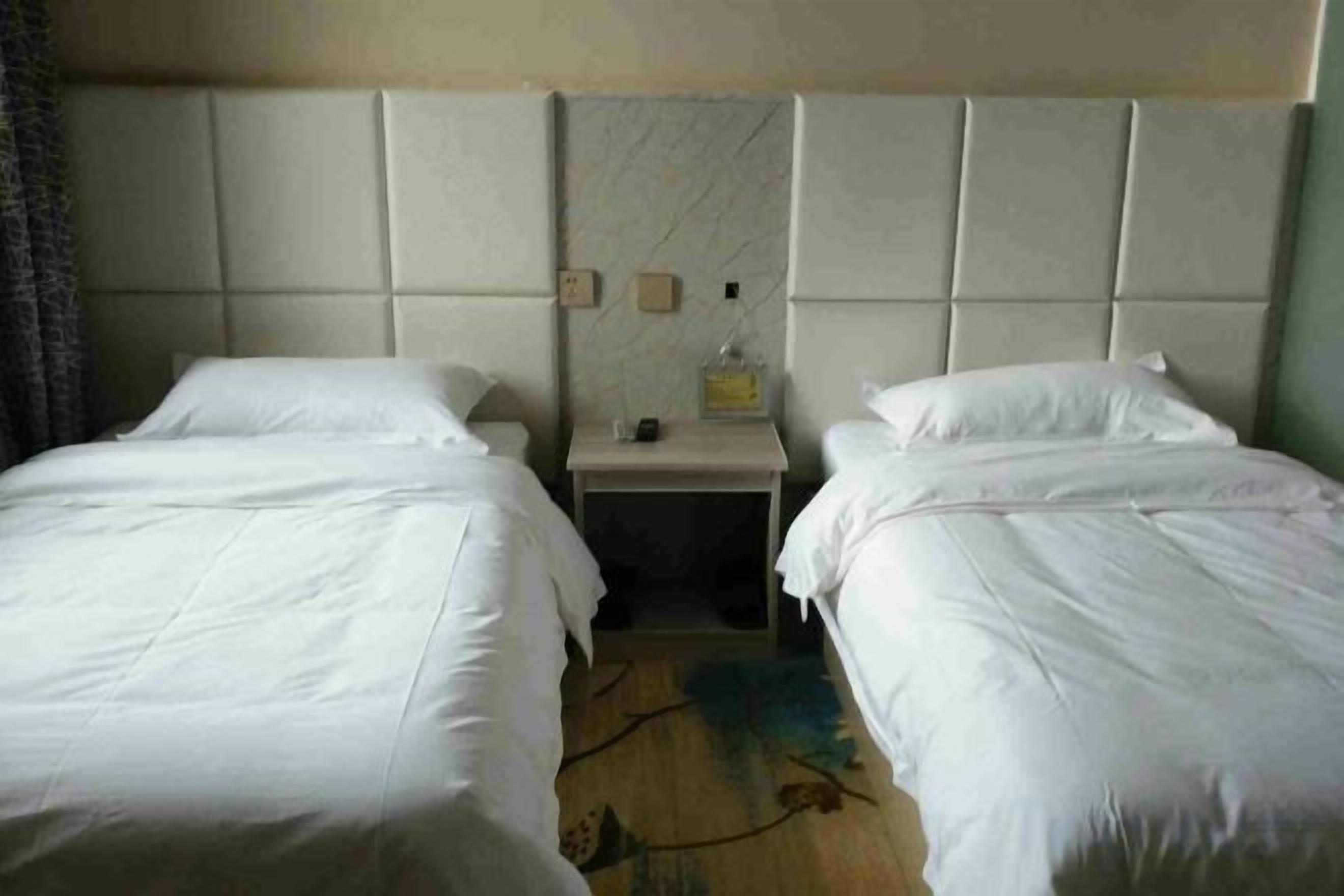 A hotel room with two single beds, a nightstand with a lamp, and a headboard with a built-in shelf.