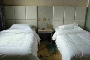Habitación de hotel con dos camas individuales, una mesita de noche con lámpara y un cabecero con estante incorporado.
