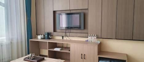 Habitación de hotel con una cama, un televisor montado en un mueble de madera, una mesita con una bandeja y una ventana con cortinas.