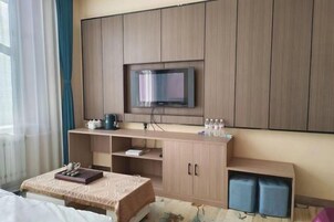 Habitación de hotel con una cama, un televisor montado en un mueble de madera, una mesita con una bandeja y una ventana con cortinas.