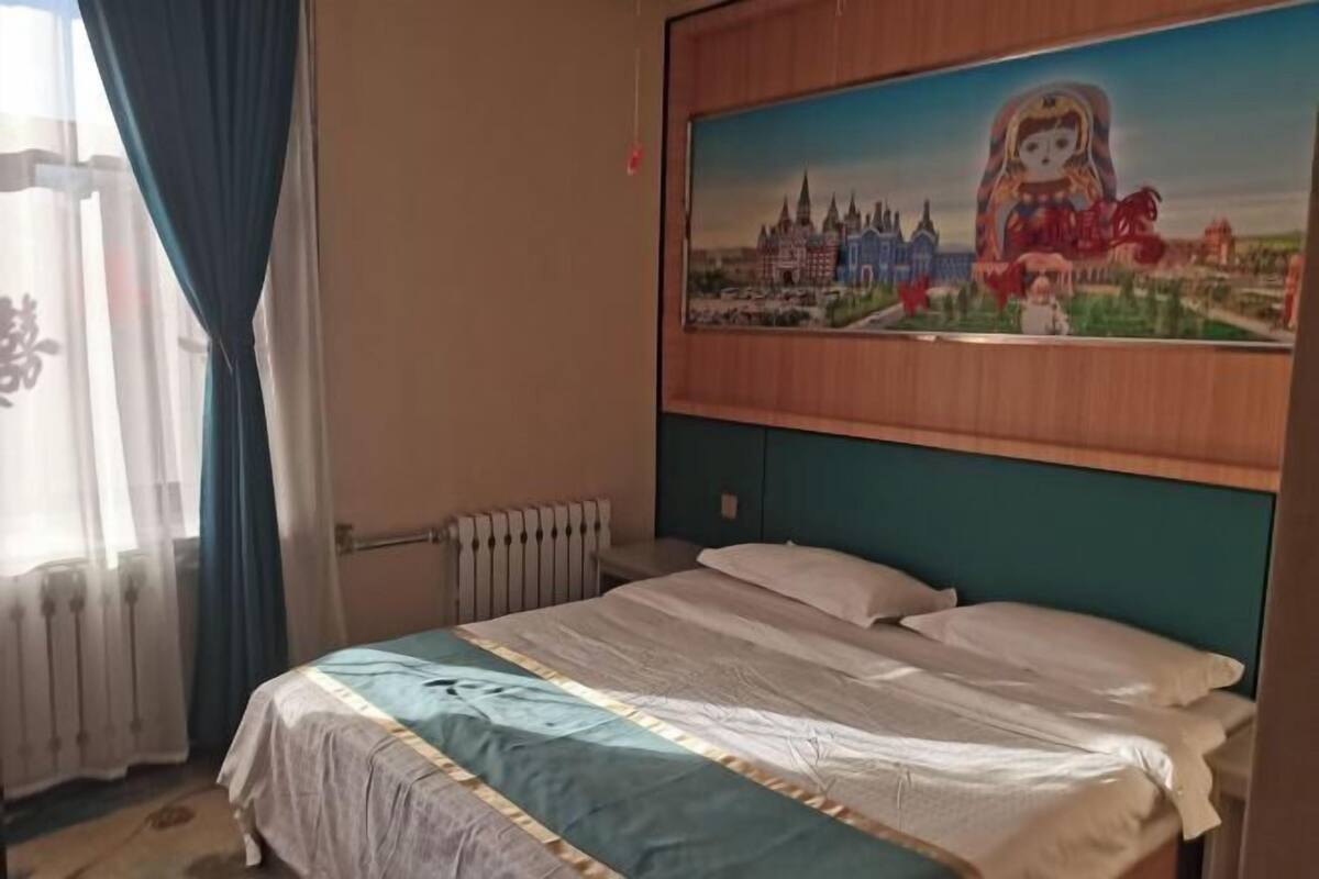 A hotel room with a bed, a radiator, a window with curtains, and a painting on the wall.