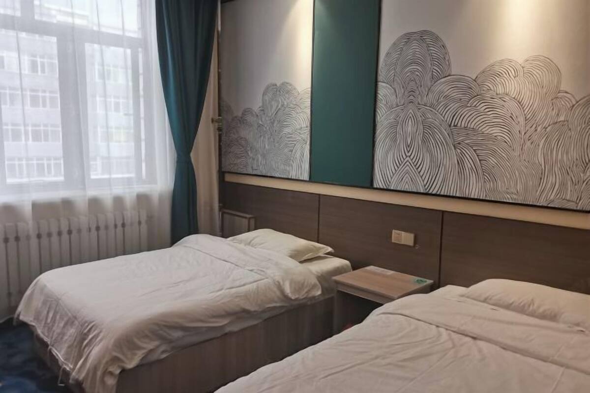 A hotel room with two single beds, a window with sheer curtains, and a wall with a large abstract art piece.