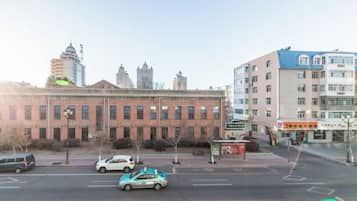 A street view with a red brick building, a bus stop, and modern high-rise buildings in the background.