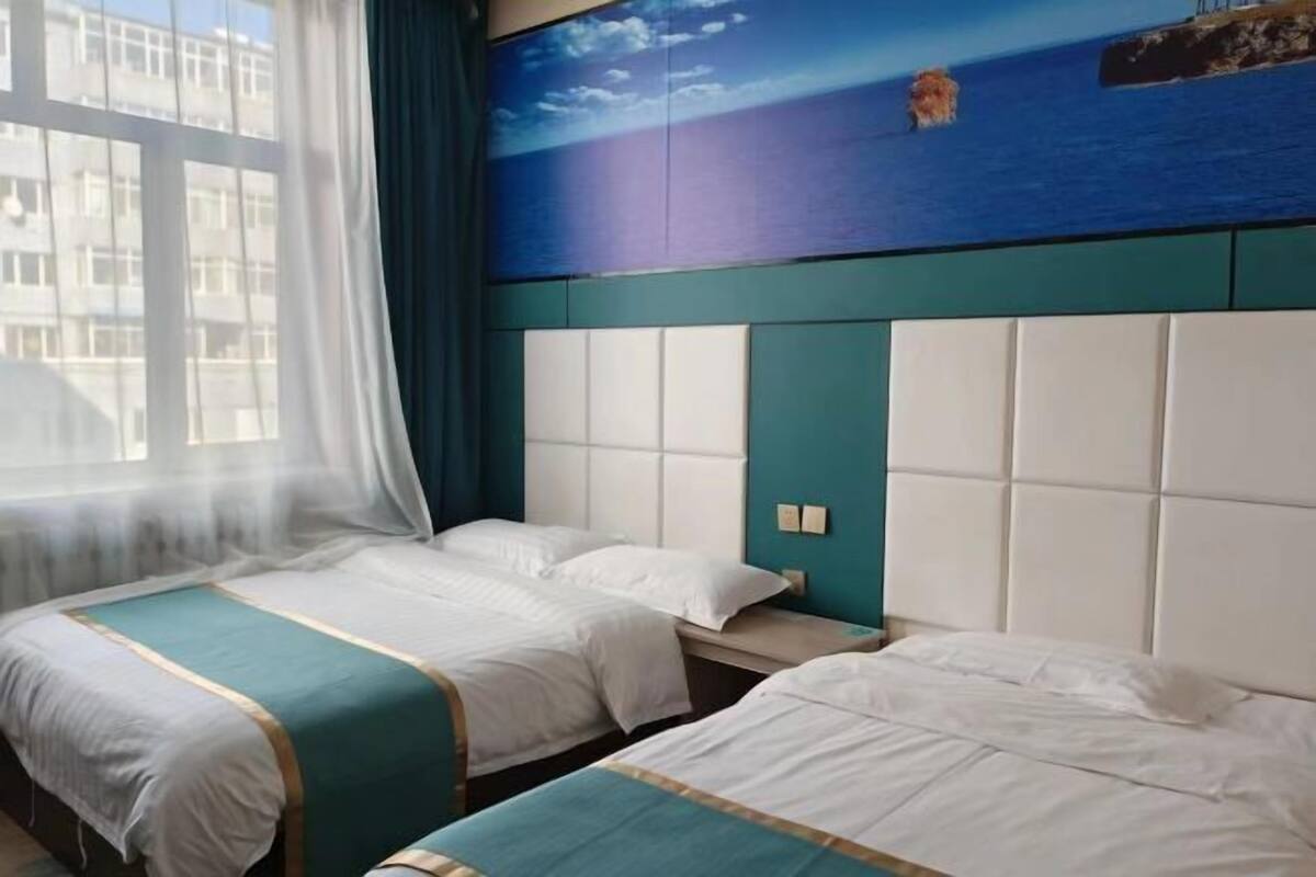 A hotel room with two beds, a large window with curtains, and a mural of a seascape on the wall.