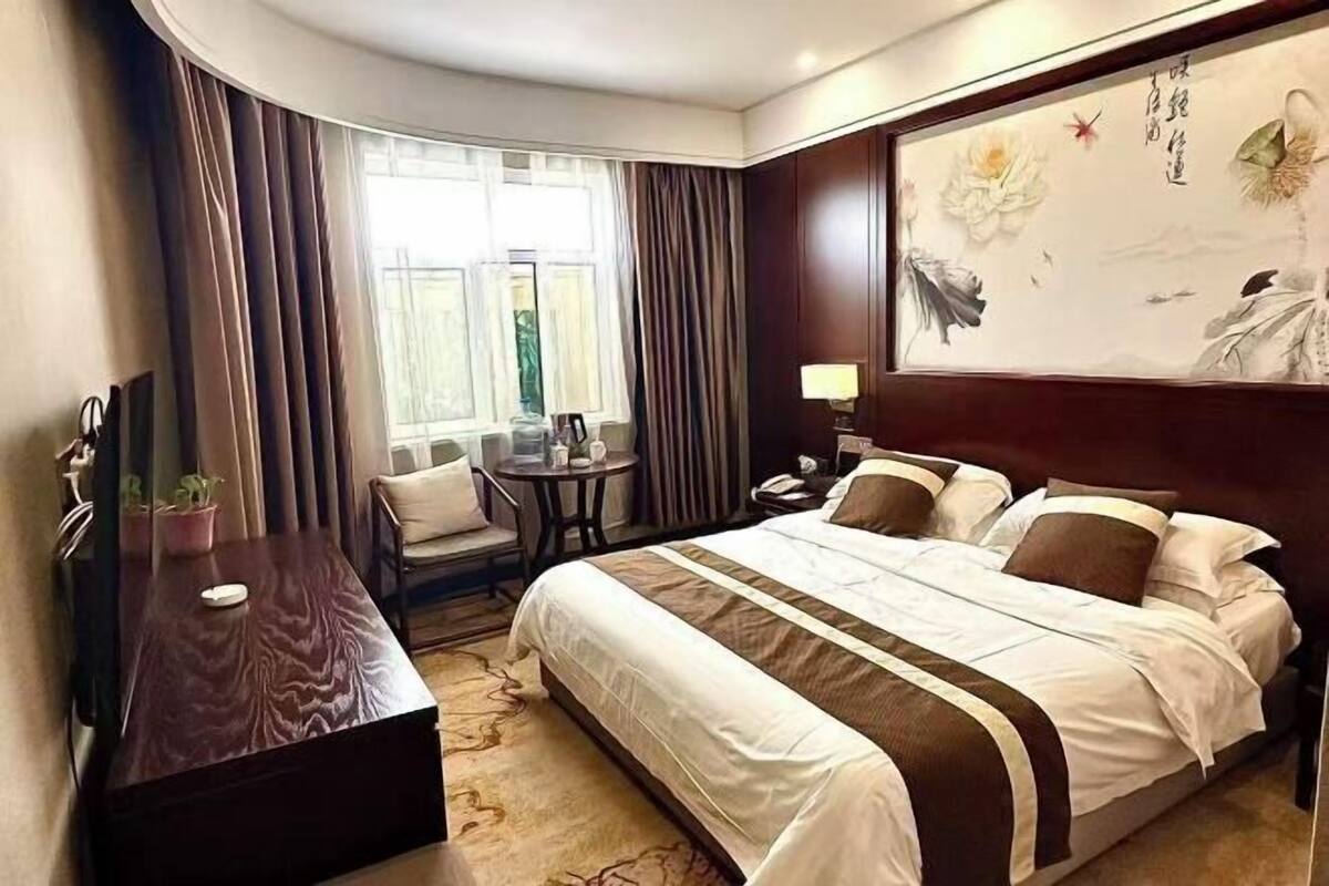A hotel room with a bed, a desk, a chair, a small table, and a window with curtains.