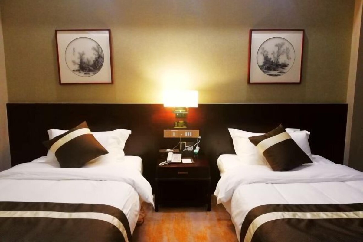A hotel room with two beds, a nightstand with a lamp, and framed artwork on the walls.