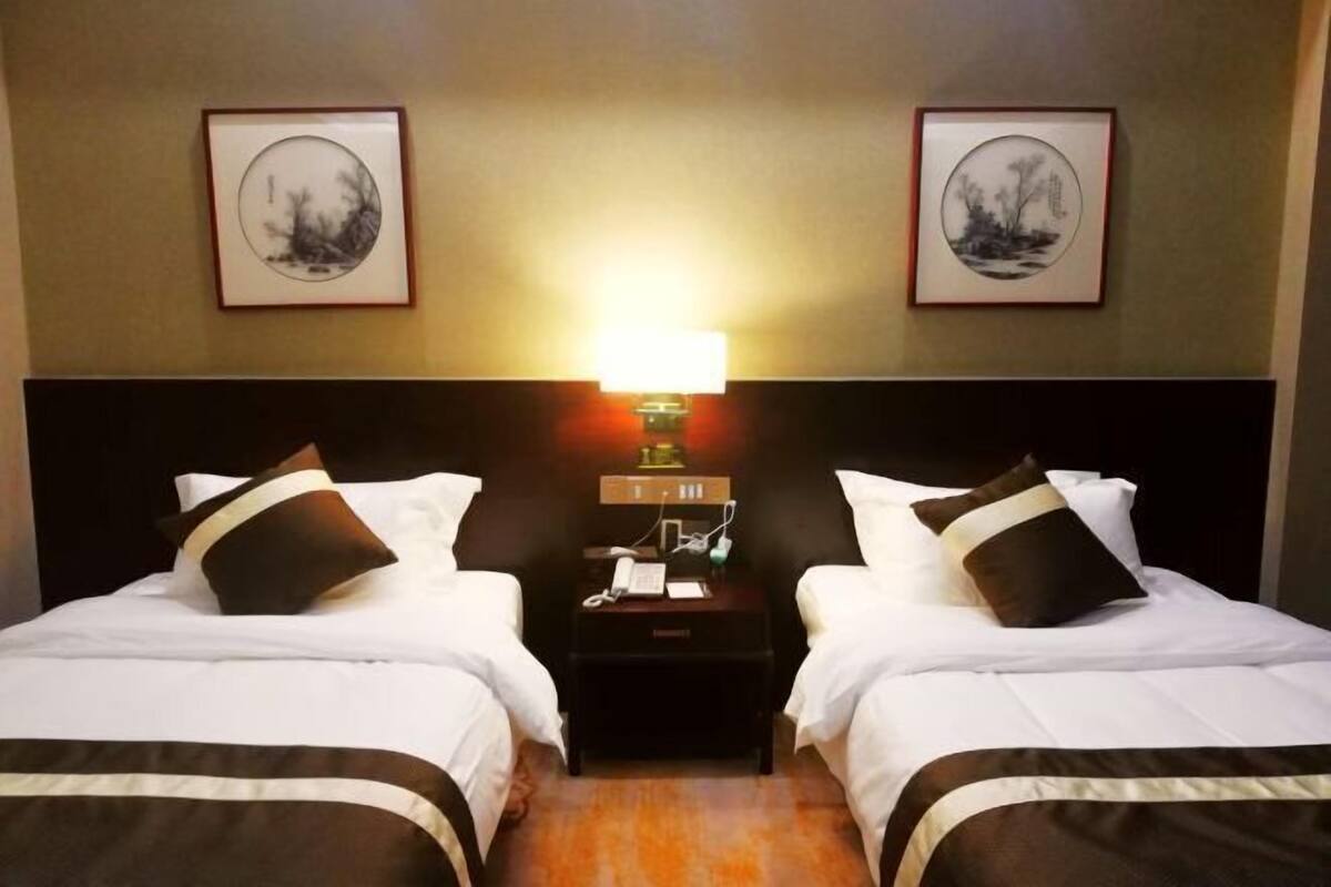 A hotel room with two beds, a nightstand with a lamp, and framed artwork on the walls.