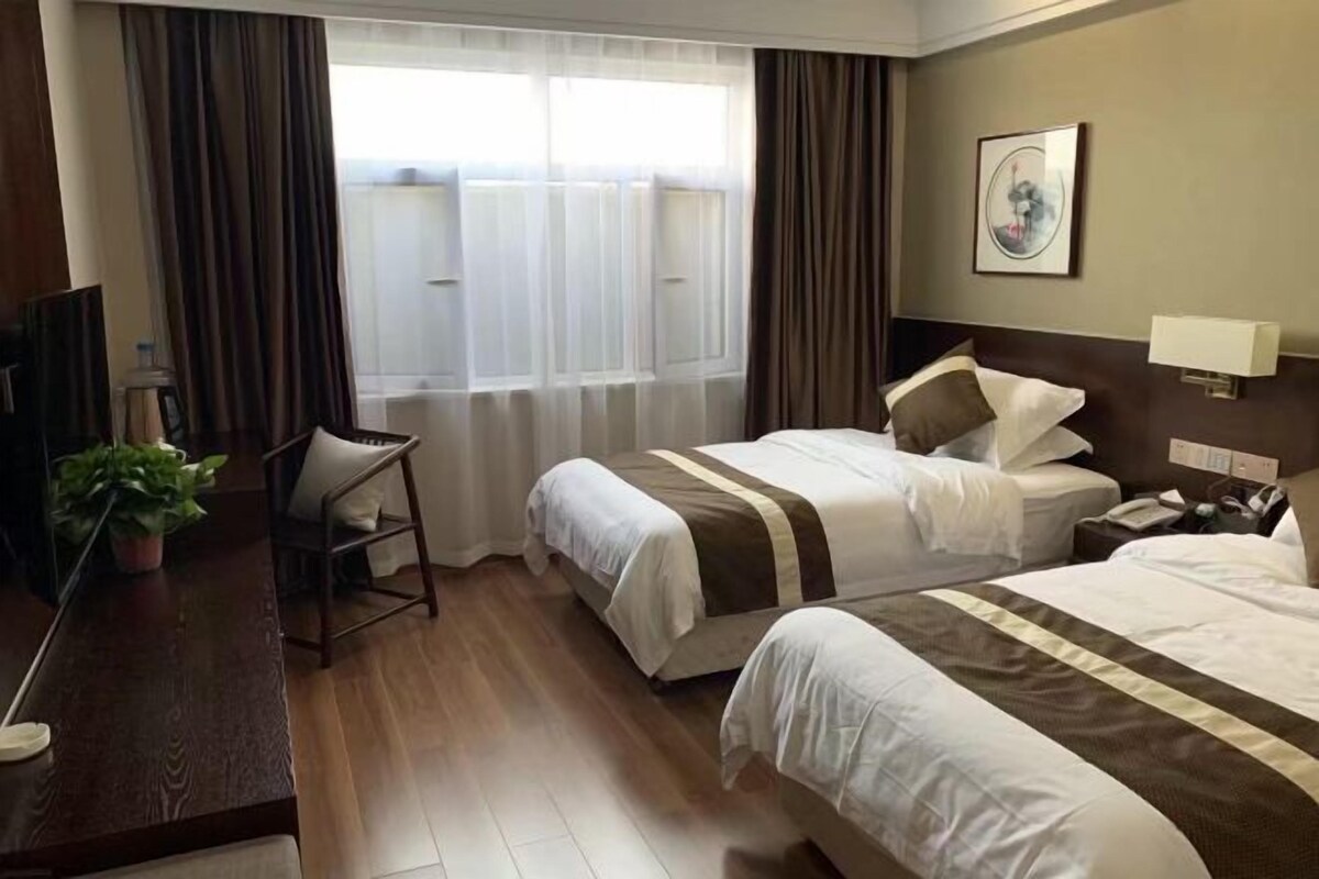 A hotel room with two beds, a desk, a chair, a TV, and a window with curtains.
