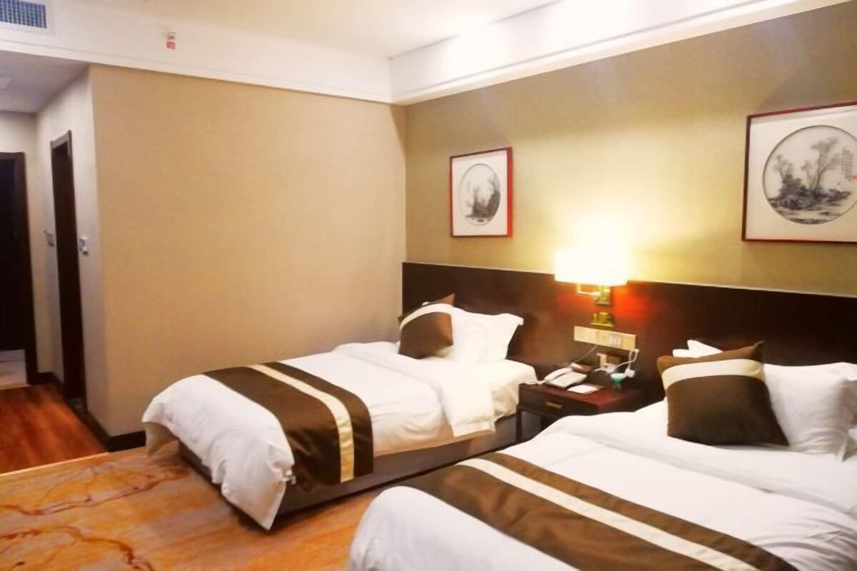 A hotel room with two beds, a nightstand with a lamp, and framed artwork on the walls.