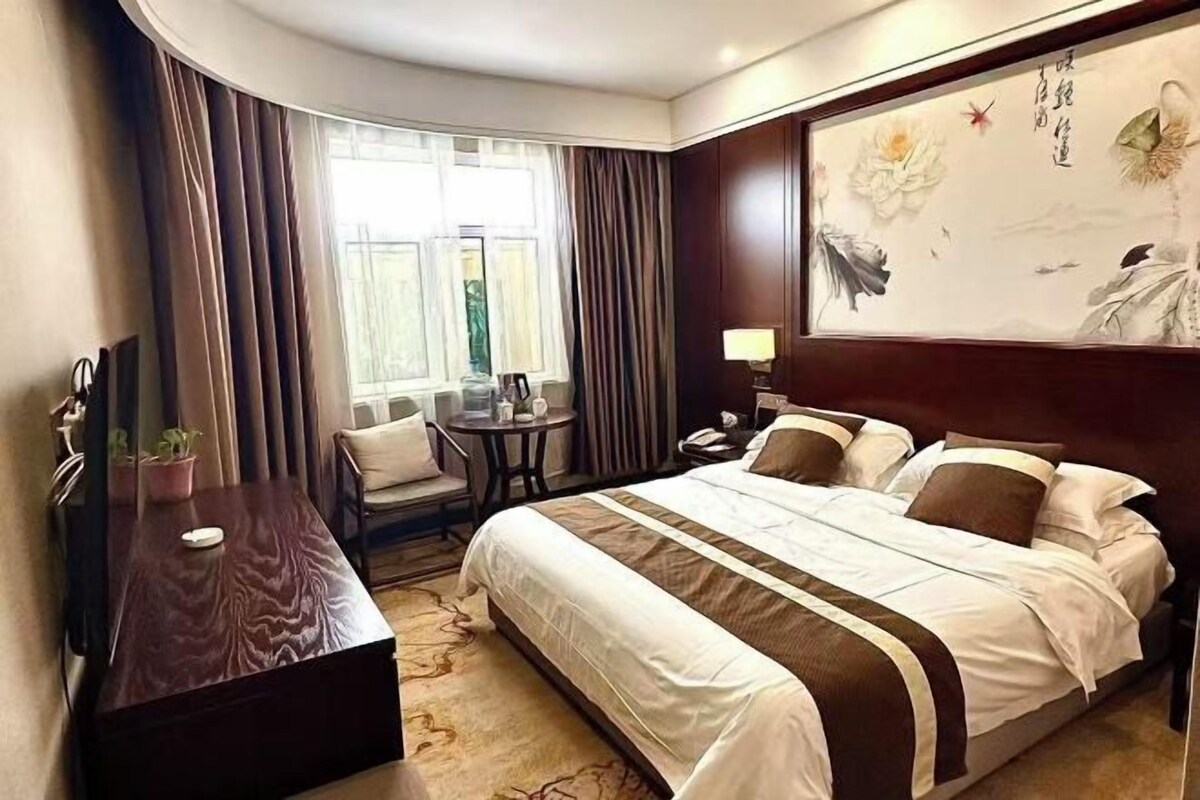 A hotel room with a bed, a desk, a chair, a small table, and a window with curtains.