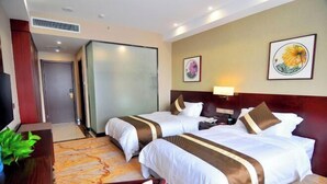 Quarto de hotel com duas camas, uma escrivaninha, televisão e obras de arte nas paredes.