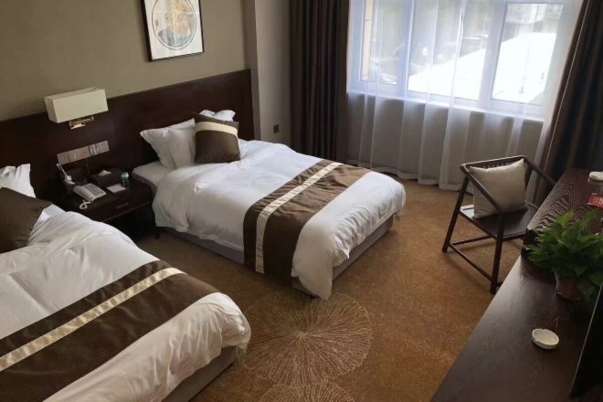 A hotel room with two beds, a desk, a chair, a lamp, and a window with curtains.