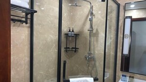 Uma casa de banho moderna com cabine de duche em vidro, um porta-toalhas preto e uma pia branca com produtos de higiene pessoal.