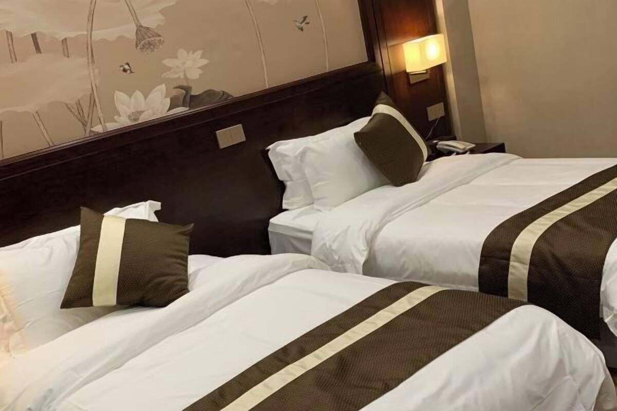 Two twin beds with white and brown bedding, a nightstand with a lamp, and a floral wall mural.
