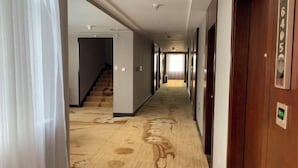 Corredor de hotel com piso carpetado, portas de madeira e escada que leva a outro quarto.